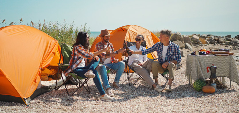 Friends camping at the beach with tents and drinks.