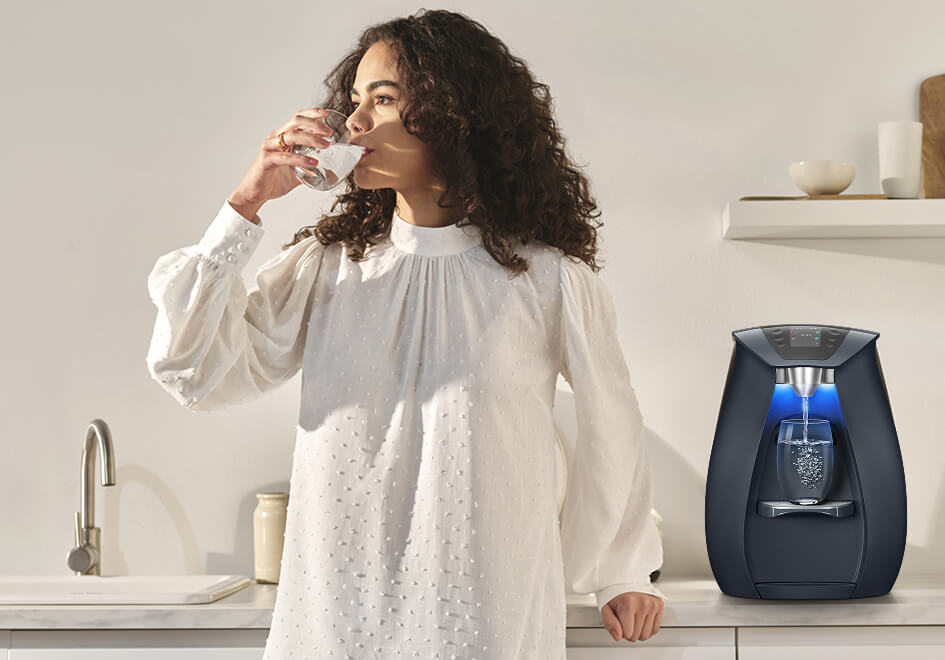 Woman drinking water near water dispenser.
