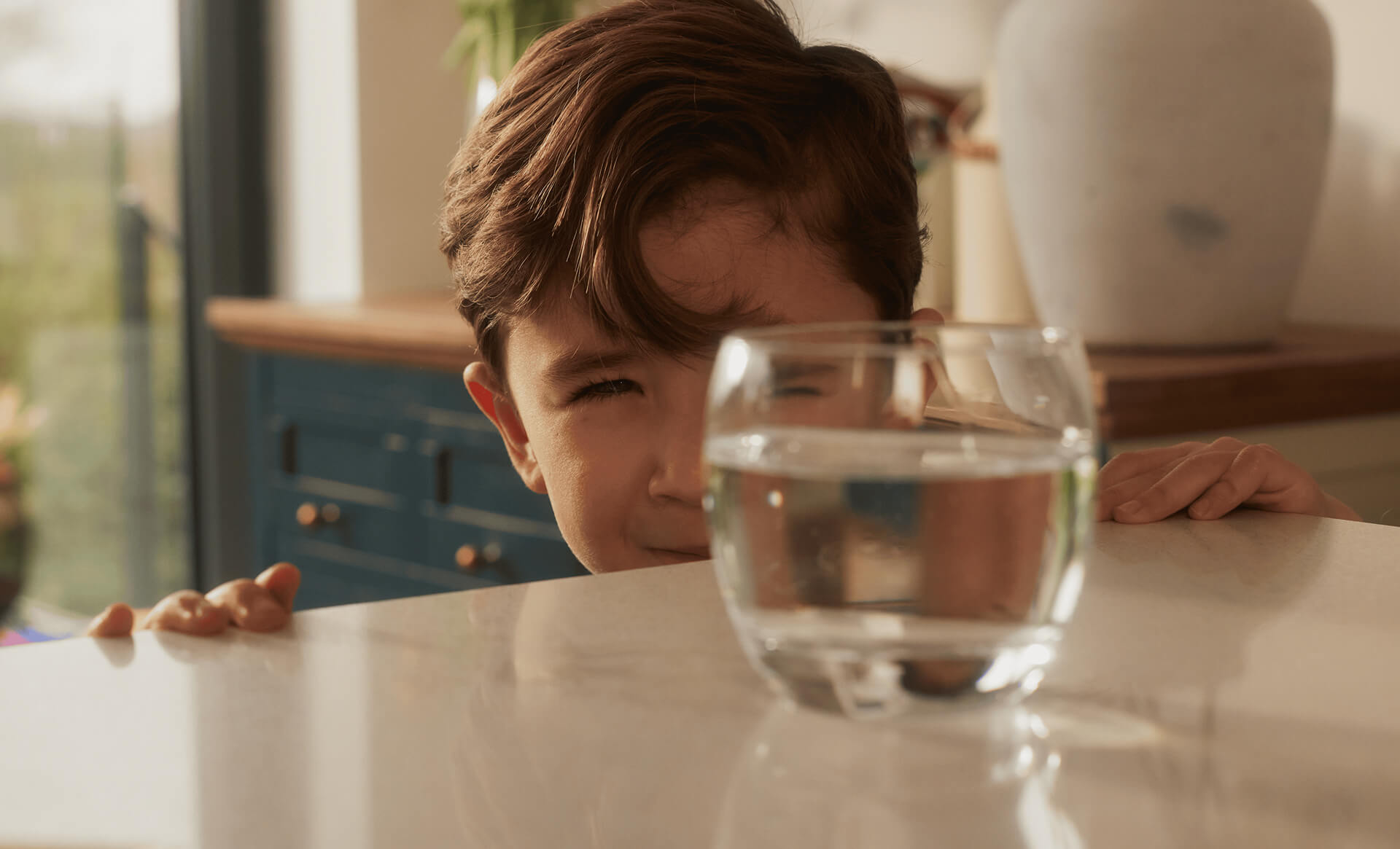 Child peeking over table at glass of water.