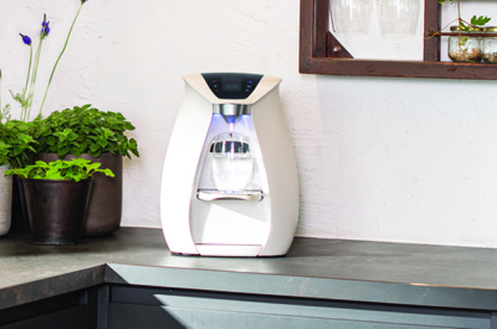 Modern countertop water dispenser next to potted plants.