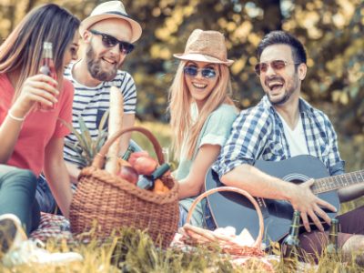 Friends enjoying picnic with guitar and food basket.